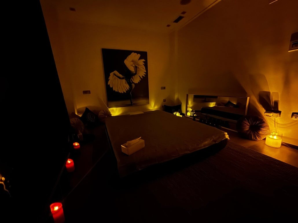 Sala de masaje con cama baja, un cuadro y velas encendidas en el suelo