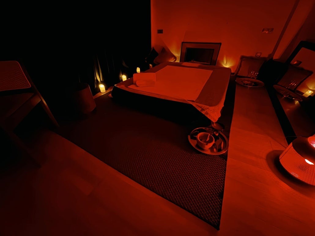 Sala de Sofía Masajes en Murcia en penumbra roja, con velas encendidas junto a la cama de masaje